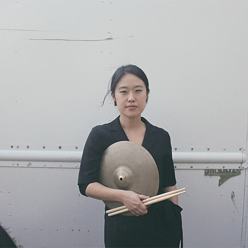 Photo of woman holding drumsticks and a cymbal (Mili Hong)