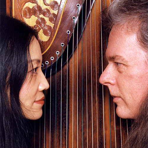 Photo of man and woman looking at each other with a string instrument in the background (RandyRR and Mei Han)