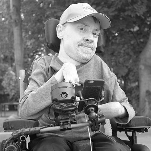 Black and white photo of man sitting down, looking at the camera (Chris Binkowski, BuckoArtMachine)
