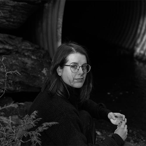 Black and white photo of a woman with glasses, looking at the camera (Emily Kennedy)