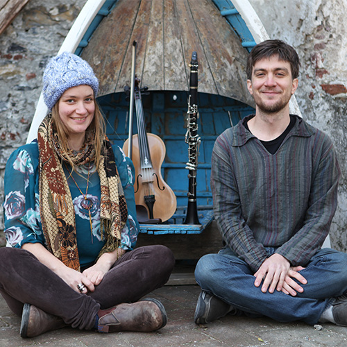 Photo of a man and a woman sitting cross-legged in front of a violin and a clarinet (Emilyn Stam and John David Williams)