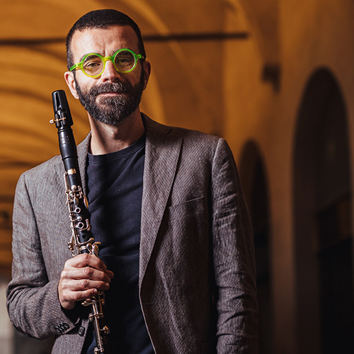 Photo of man with green glasses looking at the camera, holding a woodwind instrument (Francesco Ganassin)