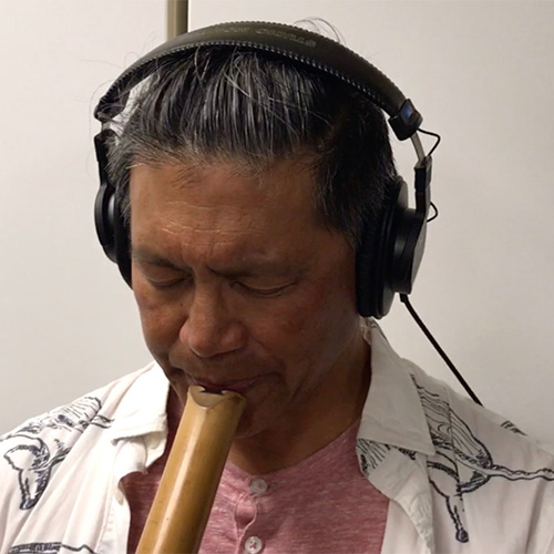 Photo of man wearing headphones, looking away from the camera, playing a woodwind instrument (James Harley)