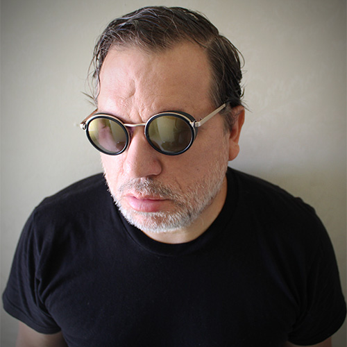 Photo of man with round black tinted glasses, looking away from camera (Rob Mazurek)
