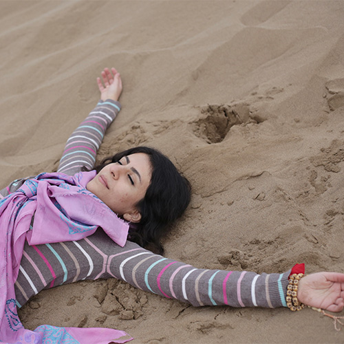 Photo of woman lying down on the sand, with closed eyes and hands outstretched (Shaghayegh Yassemi)