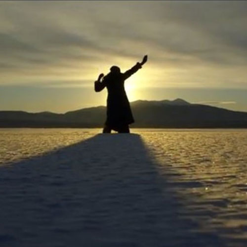 The silhouette of a dancing woman raises their arms during a sunset, surrounded by arctic snow.
